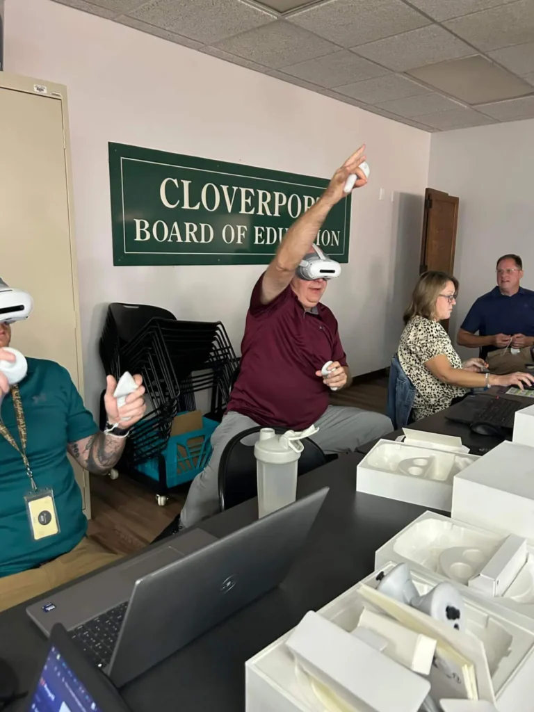 A group of people at a board meeting engage with VR headsets, some gesturing with controllers.