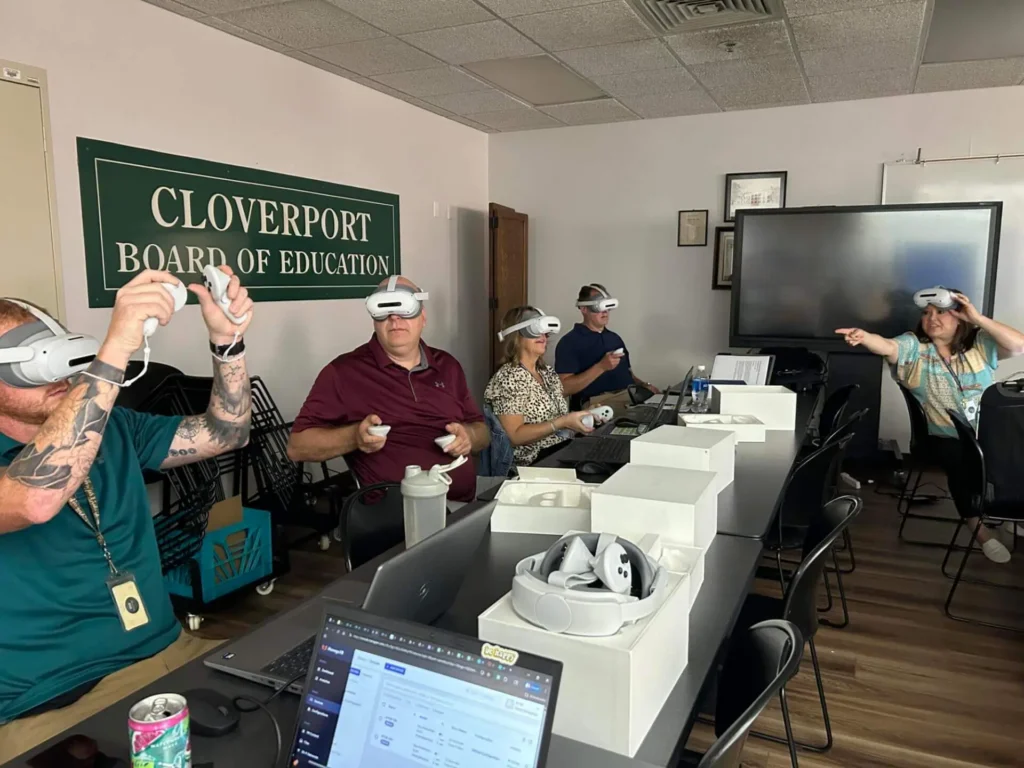 A group of people wearing virtual reality headsets sits around a conference table in a board room. 