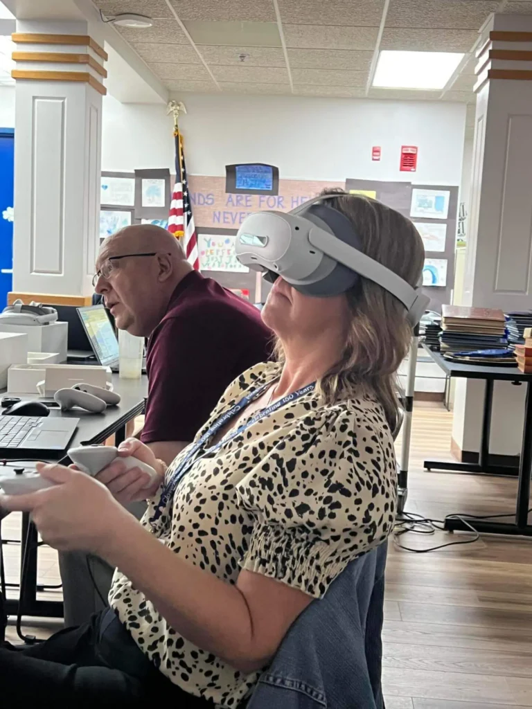 A woman wearing a virtual reality headset sits beside a man in an office-like setting. 